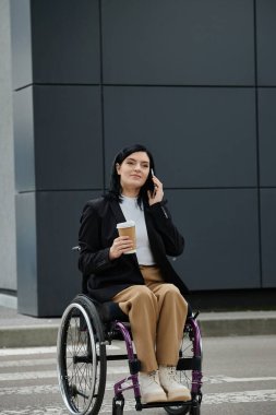 Tekerlekli sandalyedeki bir kadın elinde kahve tutarken telefonla konuşuyor..