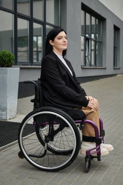 Tekerlekli sandalyedeki bir kadın binanın dışında oturuyor ve yukarı bakıyor..