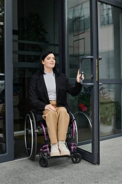 Tekerlekli sandalyedeki bir kadın binanın kapısını açıyor..