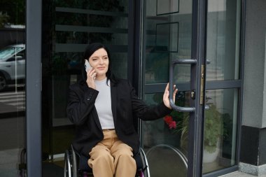 Tekerlekli sandalyedeki bir kadın binaya girerken telefonunu kullanıyor..