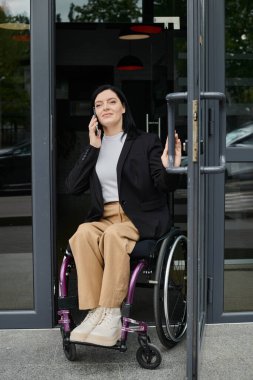 Tekerlekli sandalyedeki bir kadın telefonda konuşurken binaya giriyor..