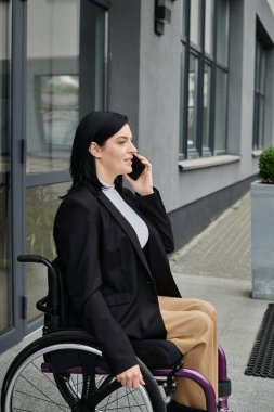 Spor ceketli ve bej pantolonlu bir kadın telefonda konuşuyor.