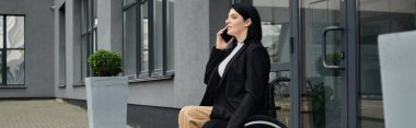 Tekerlekli sandalyedeki bir kadın binanın dışında oturuyor ve telefonuyla konuşuyor..