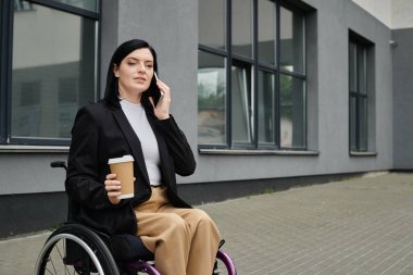Tekerlekli sandalyedeki bir kadın ofis binasının önünde oturmuş telefonla konuşuyor..