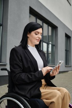 Binanın dışında tekerlekli sandalyede oturan bir kadın telefonuna bakıyor..