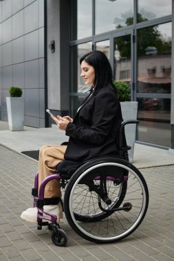 Tekerlekli sandalyedeki bir kadın telefonunu binanın dışında kullanıyor..