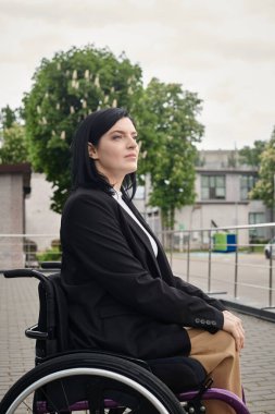 Tekerlekli sandalyedeki bir kadın şehir caddesinde oturuyor, düşünceli bir şekilde uzaktan bakıyor..
