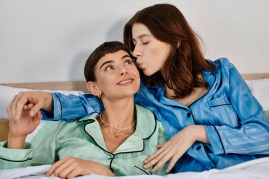 Genç lezbiyen bir çift yatakta pijama giyer, hassas bir anı paylaşır..