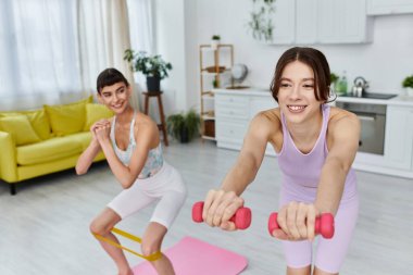 Spor giyim sektöründe iki kadın modern bir dairede birlikte çalışıyor. Biri direniş bandı kullanıyor, diğeri ağırlık kaldırıyor..
