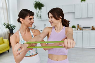 Geniş bir dairede spor giyinen iki kadın birlikte spor yapıyor..