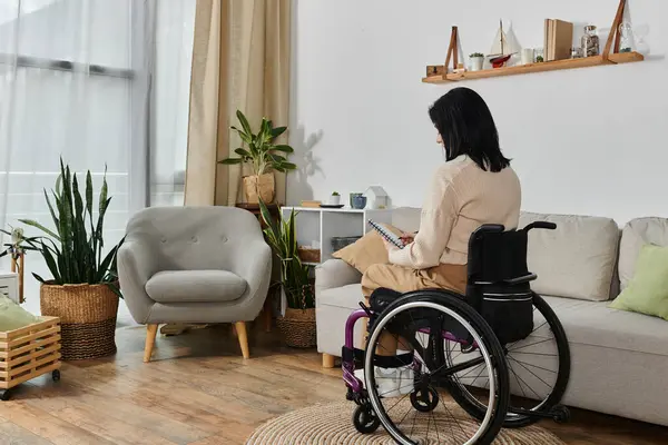 stock image A woman in a wheelchair sits in a living room, reading a book.