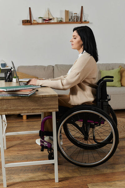 Женщина в инвалидной коляске работает на ноутбуке за столом в своем доме.