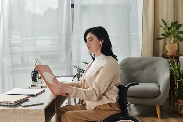 stock image A woman in a wheelchair sits at a desk, studying a book.