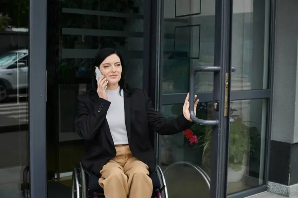 stock image A woman in a wheelchair uses her phone while entering a building.