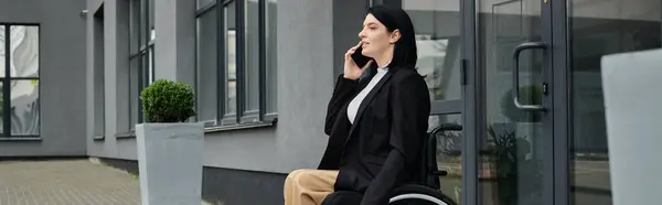 stock image A woman in a wheelchair sits outside a building, talking on her phone.