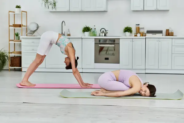 stock image Two women in athletic wear practice yoga poses in a modern apartment kitchen.