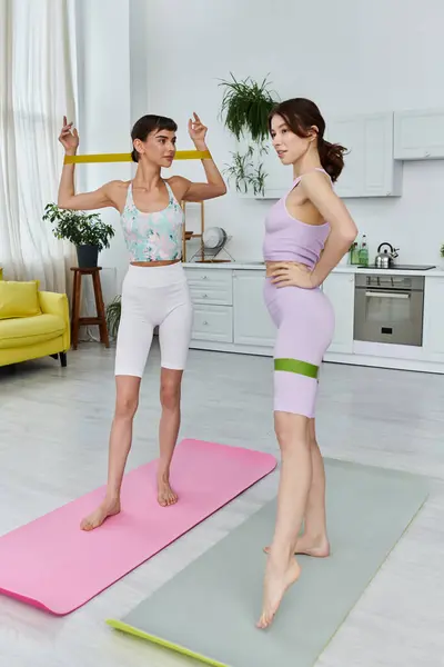 stock image Two young women in sportswear use resistance bands during a workout session on yoga mats in a modern apartment.