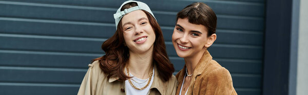 Two women, dressed in trendy outfits, smile brightly as they walk together outdoors.