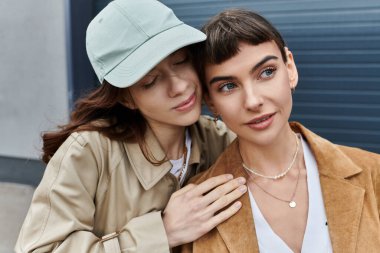 Moda kıyafetleri içinde iki genç kadın şehir manzarasıyla çevrili açık havada hassas bir anı paylaşıyor..