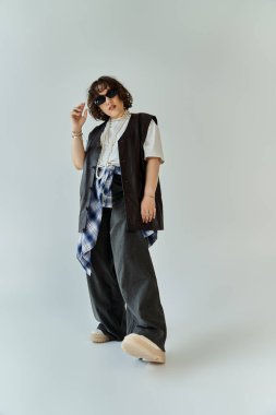 Beyaz tişört ve geniş paçalı pantolonun üzerine siyah yelek giyen bir kadın kendine güvenerek poz verir..