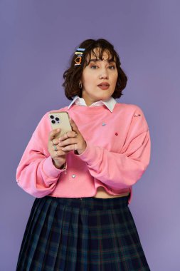 Pembe kazaklı ve ekose etekli genç bir kadın telefonu tutuyor. Yüzündeki ifade düşünceli..