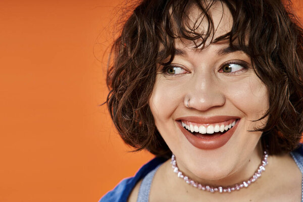 Женщина в ярко синем топе ярко улыбается на тёплом оранжевом фоне.