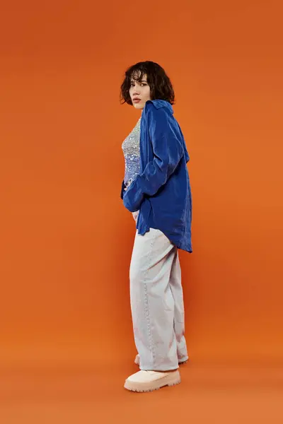 stock image A woman stands in front of an orange backdrop, wearing a blue shirt and white pants.