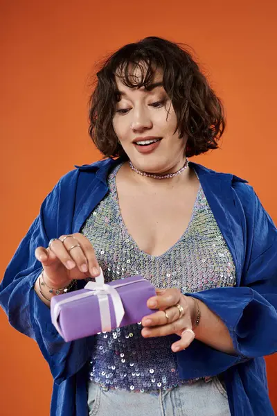 stock image A woman in a colorful outfit opens a gift with a smile on her face.