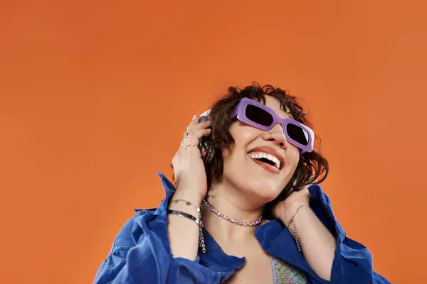 stock image A woman in a blue shirt and sunglasses smiles and listens to music.