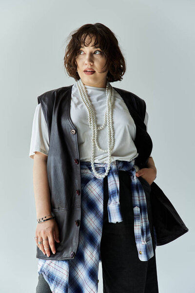 A woman in a leather vest, plaid shirt, and pearl necklace looks thoughtfully off-camera.