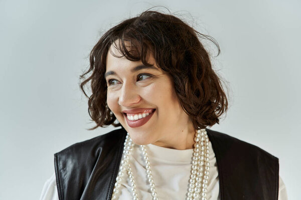 Женщина в черном жилете с жемчужным ожерельем улыбается и смотрит не в камеру.