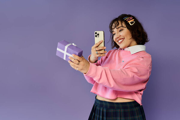 Молодая женщина улыбается, делая селфи с фиолетовой подарочной коробкой и телефоном
