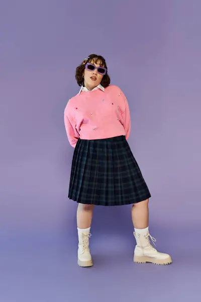 stock image A woman in a pink sweater and plaid skirt poses against a lavender backdrop.