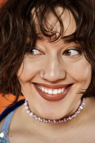 Женщина с темными вьющимися волосами ярко улыбается, одетая в красочное ожерелье.