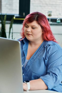 A plus size woman with pink hair works intently on a laptop. clipart