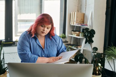 A plus size businesswoman with pink hair, focused on her notebook, sits at a desk in a bright office. clipart