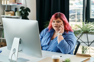 A plus size woman in blue sits at a desk and speaks on a phone. clipart