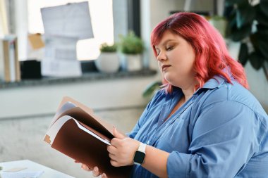 Pembe saçlı, iri yarı bir kadın ofiste otururken dokümanları inceliyor..