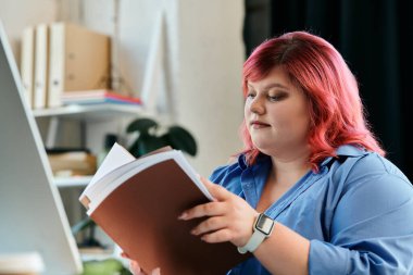 Pembe saçlı iri yarı bir kadın bir kitap okuyor, düşüncelere dalmış..