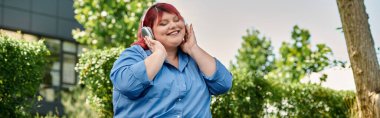 Güzel bir bahçede müzik dinlerken kızıl saçlı iri bir kadın gülümsüyor..