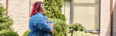 A plus size woman in a vibrant blue shirt stands outside with her arms crossed, gazing upward. clipart