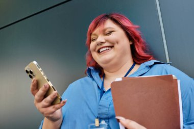 Parlak pembe saçlı iri yarı bir kadın telefonuna bakarken gülüyor..