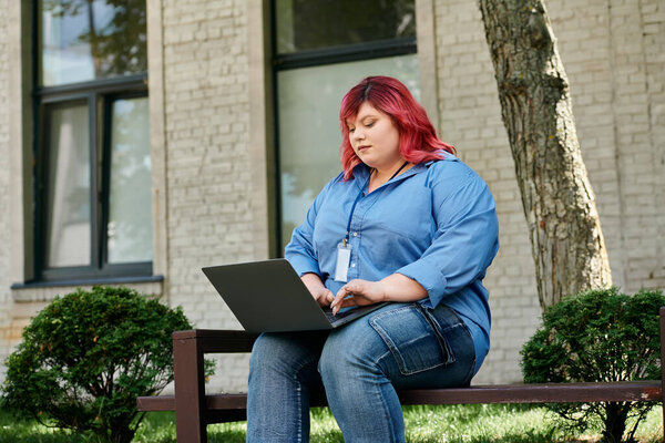 Женщина plus size в яркой одежде использует ноутбук, сидя на скамейке снаружи.