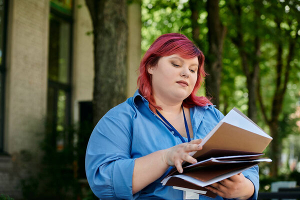 A plus size woman in a blue shirt and pink hair reads through a stack of documents outside.