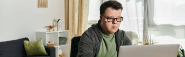 man with Down syndrome focuses intently on his laptop in a cozy, well lit room. clipart