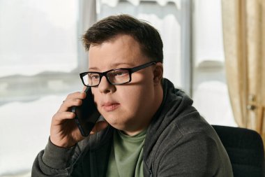 A young man with Down syndrome is focused on a phone conversation in a cozy home environment. clipart