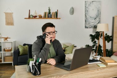 Down sendromlu genç bir adam masasında otururken telefonla konuşuyor..