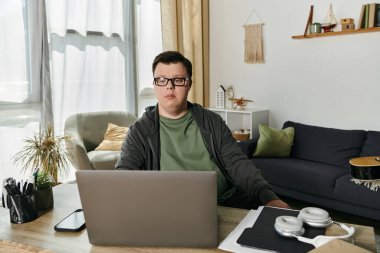 Down sendromlu genç bir adam rahat evinde çevrimiçi öğrenim seansına katılıyor..