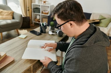 A man with Down syndrome explores the pages of a book in his cozy living space. clipart