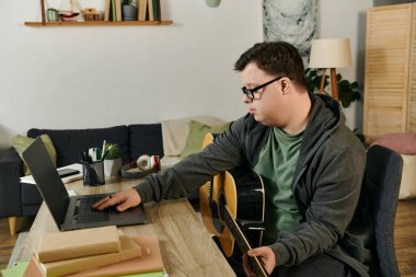 Down sendromlu genç bir adam dizüstü bilgisayarını kullanırken gitarıyla meşgul oluyor..